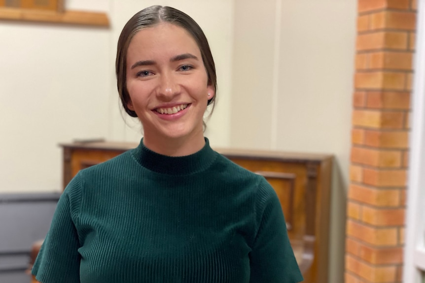 Young woman in green shirt smiling in front of a piano. Ausnew Home Care, NDIS registered provider, My Aged Care