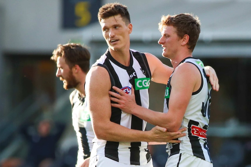 Two Collingwood Magpies AFL players embrace as they celebrate a goal against Carlton.