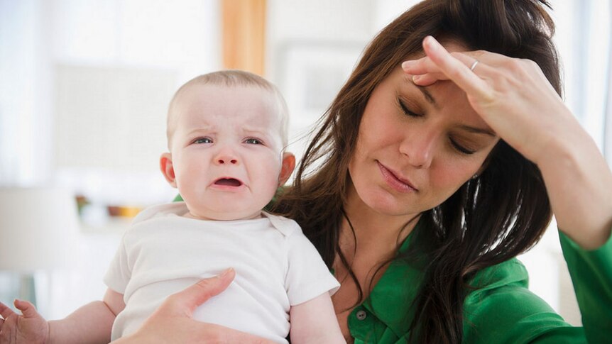 A mother holding her crying baby looks frustrated.