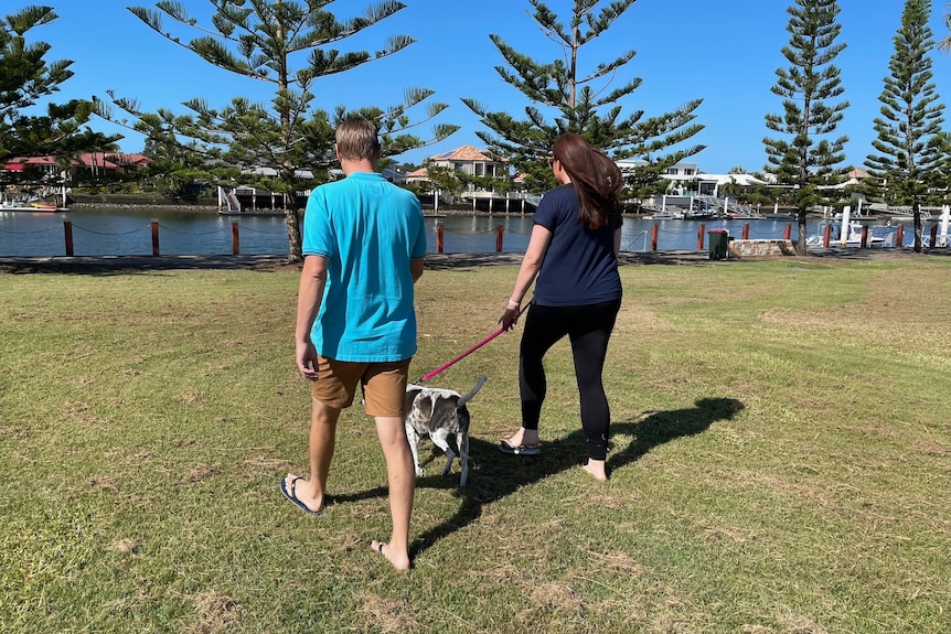 man, woman and dog walk in the park near a canal