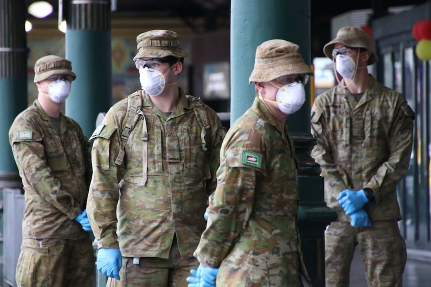 Four ADF officers wearing masks and blue gloves stand in a group.