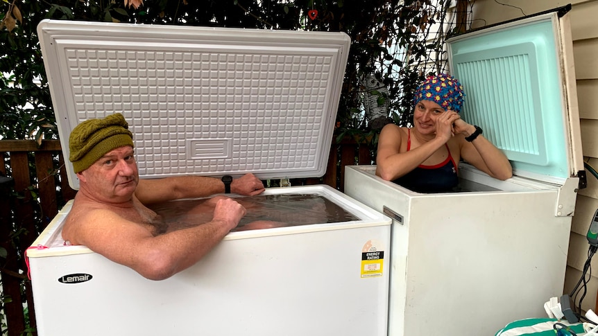 Two swimmers sit inside individual deep freeze tubs filled with ice water