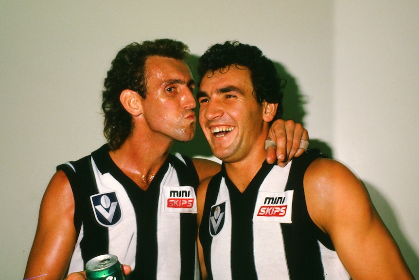 Peter Daicos pretends to kiss Darren Millane on the cheek while holding a beer.