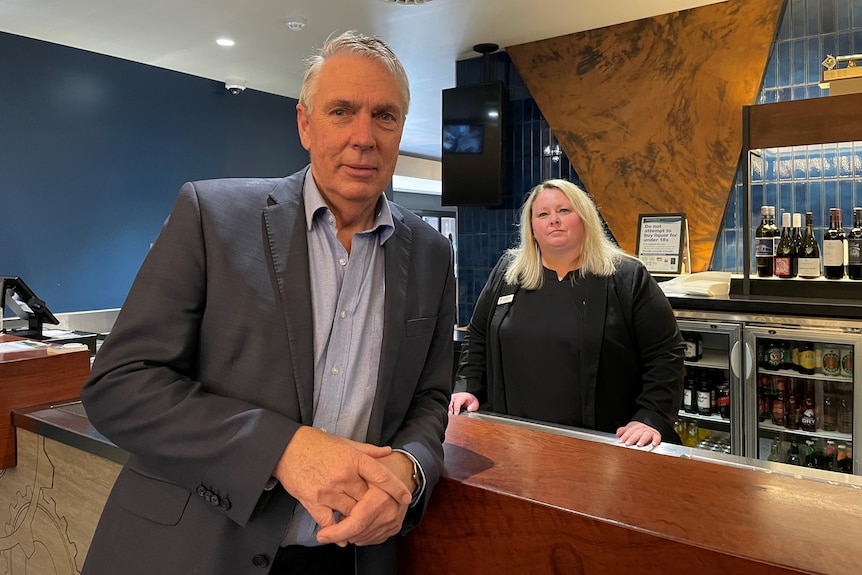 A man leaning on a bar and a woman standing behind the bar.