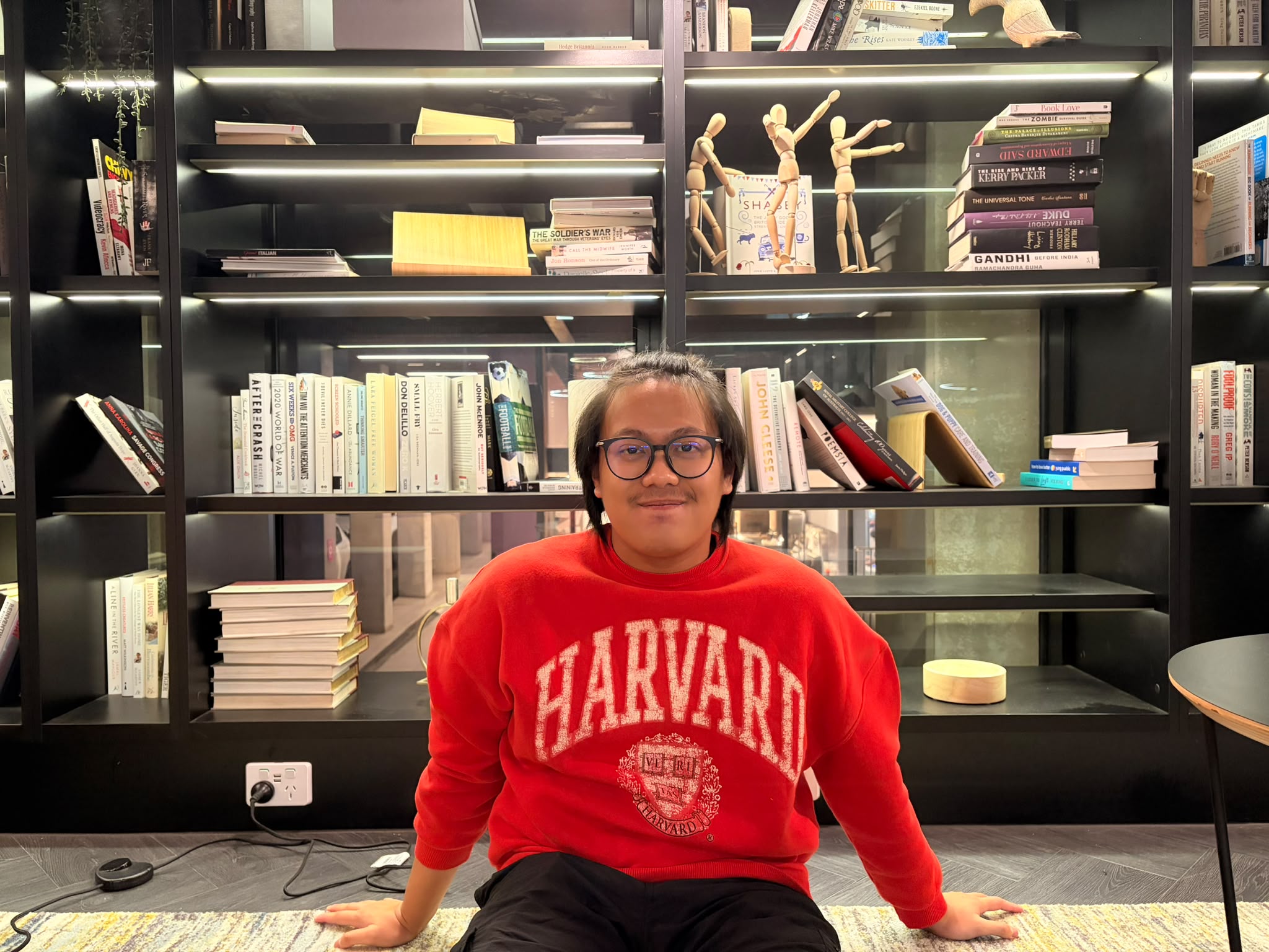 A man in glasses sitting in front of a book shelf.