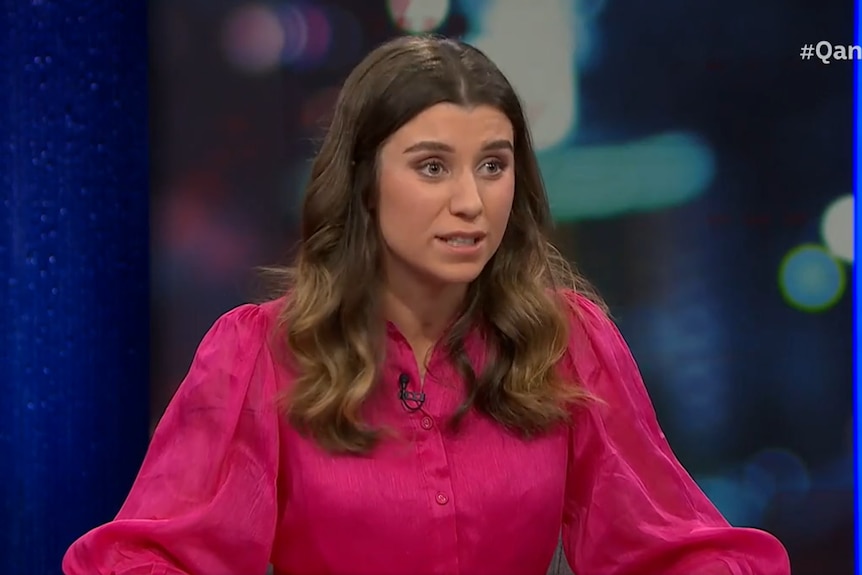 A young woman in a pink dress speaks on the Q+A set.