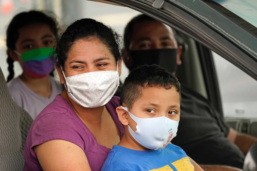 A mother wearing a mask holds her son, also wearing one ahead of a coronavirus test.