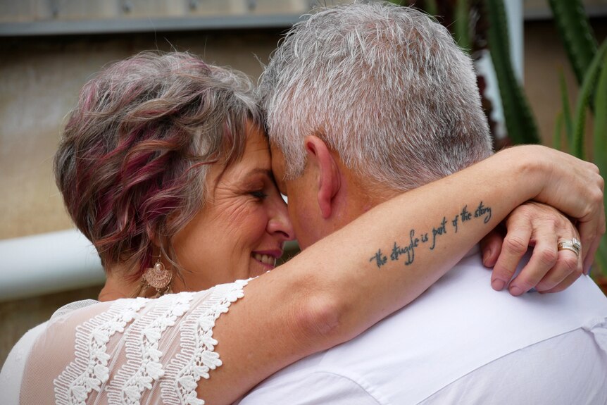A man and woman embrace. The woman has a tattoo on her arm that says 'the struggle is part of the story'