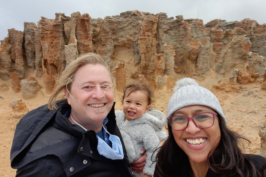 A Caucasian man and Indonesian woman holding with their child doing a selfie.