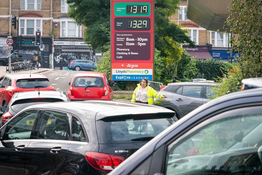 A staff member directs cars at a petrol station.