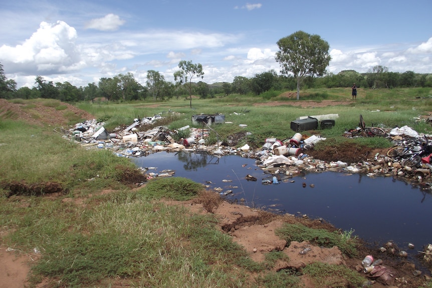 trench full of blue water and rubbish surrounded by grass