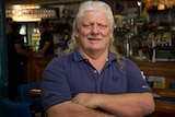 Picture of a man with long grey hair worn in a mullet, with ringlets down his shoulders.