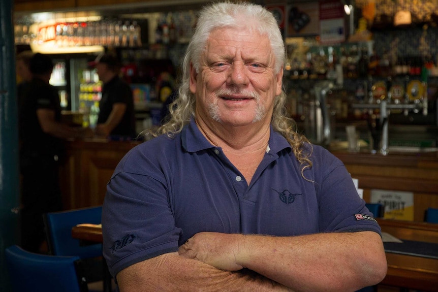 Picture of a man with long grey hair worn in a mullet, with ringlets down his shoulders.