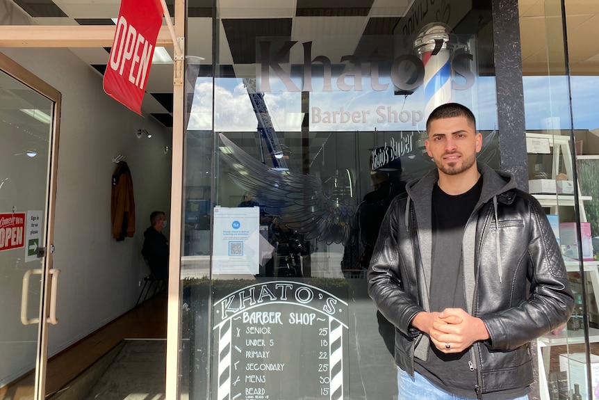 Man stands in front of barbershop.