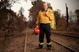 Brendon O'Connor stands on a railway line holding his RFS helmet and jacket.