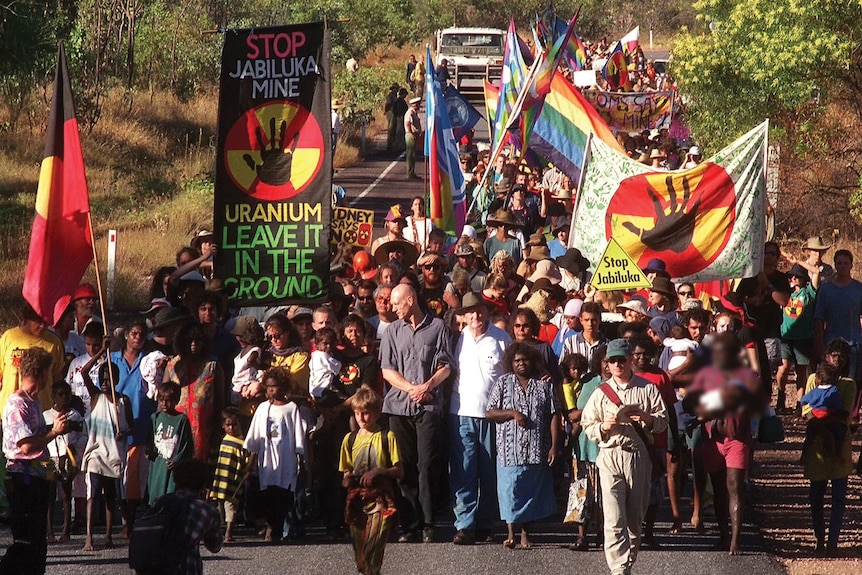 Large group of people walking along a road carrying colourful signs.