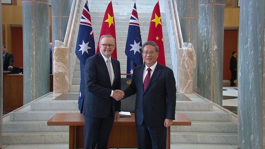 Anthony Albanese and Li Qiang shake hands in front of a wooden table, with Chinese and Australian flags behind them.