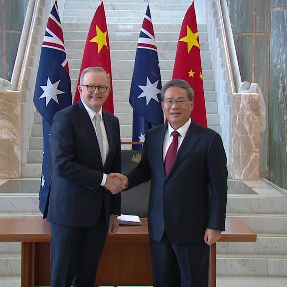 Anthony Albanese and Li Qiang shake hands in front of a wooden table, with Chinese and Australian flags behind them.