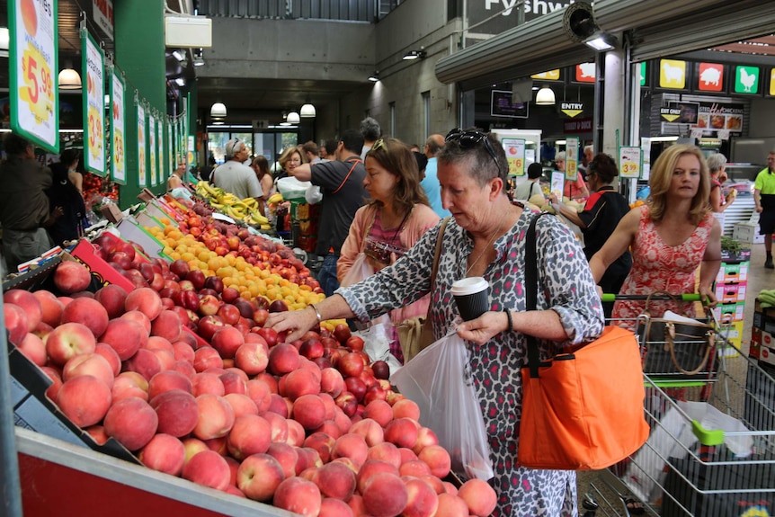 A woman looks at peaches in a busy market place.