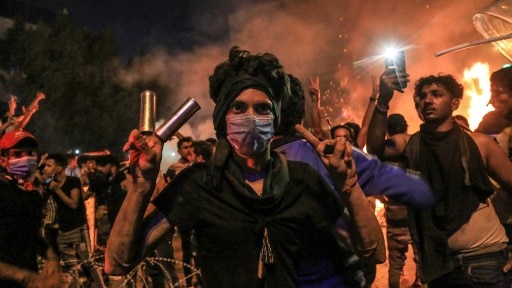 A man wearing a mask holds tear gas canisters.