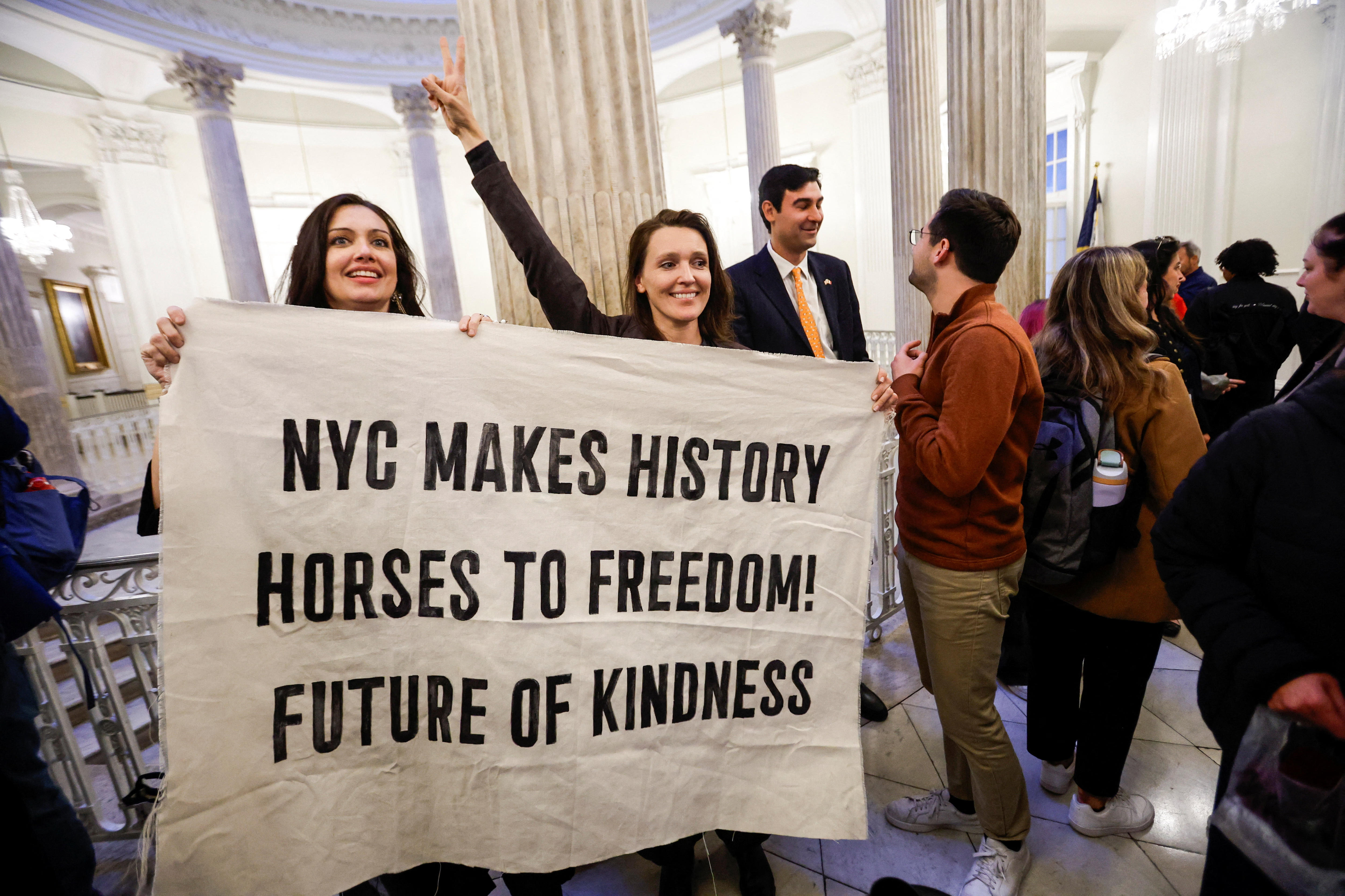 Two people hold a banner saying "NYC makes history, Horse to freedom, future of kindness".
