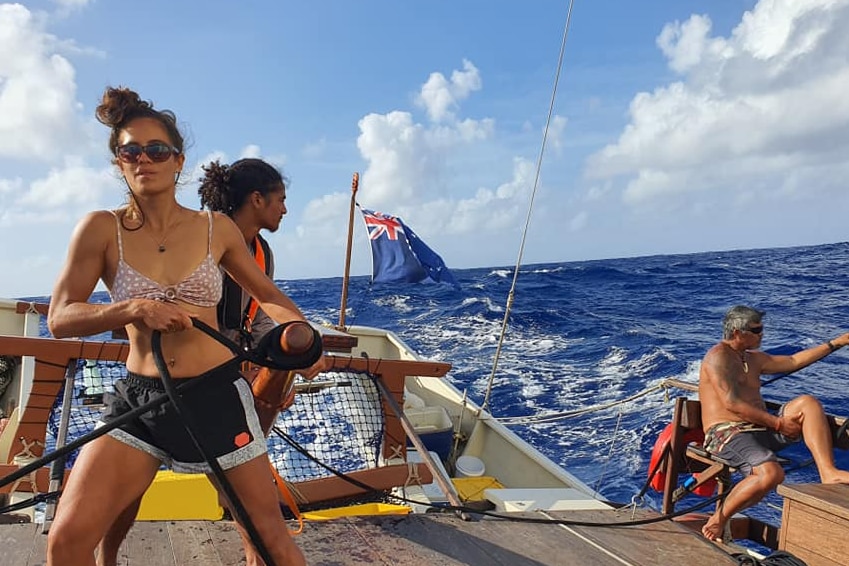 A strong Cook Island woman in a power stance sailing in the Pacific Ocean with blue water surrounding the vessel 