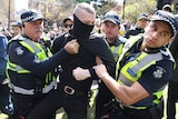 A man is taken away by Victoria Police after he refused to take off a mask during a rally in Melbourne