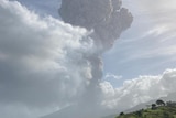 A mushroom cloud in the distance with green hills in the foreground.