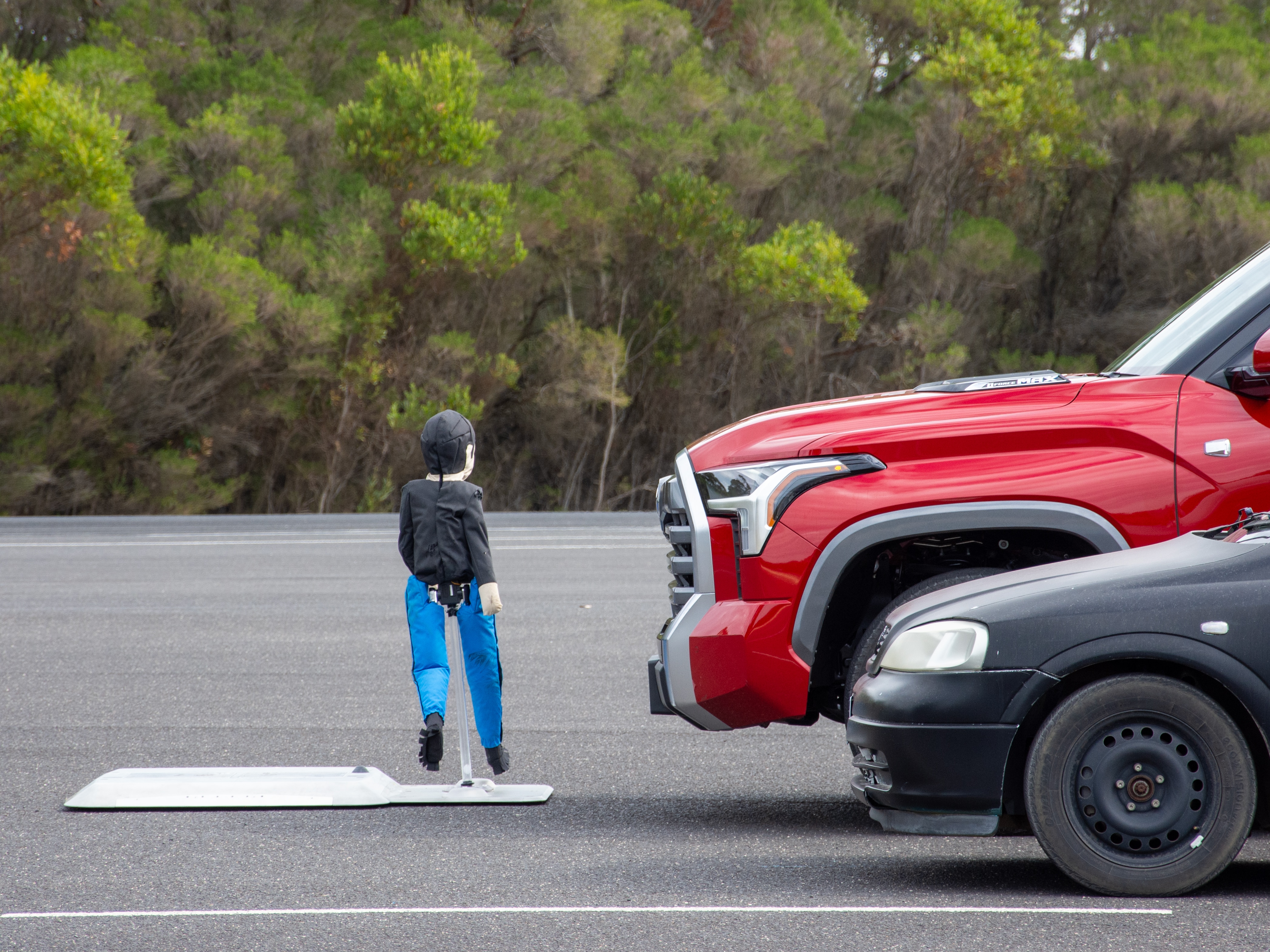 A dummy model of a child walking in front of a passenger car and a large ute