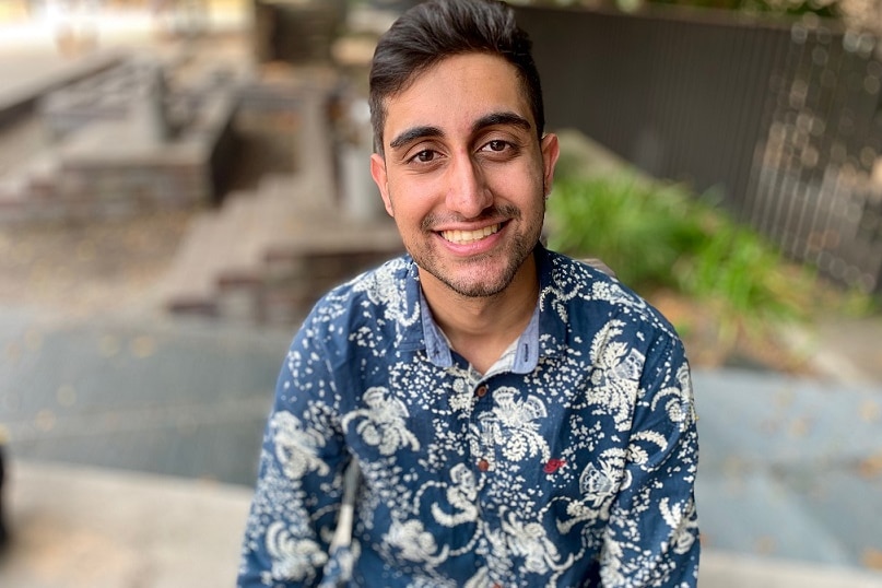 Ryan Nindra, wearing a patterned button-up shirt, smiles directly at the camera.