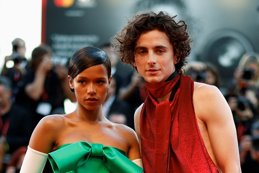 A man in red and a woman in green stare towards the camera.
