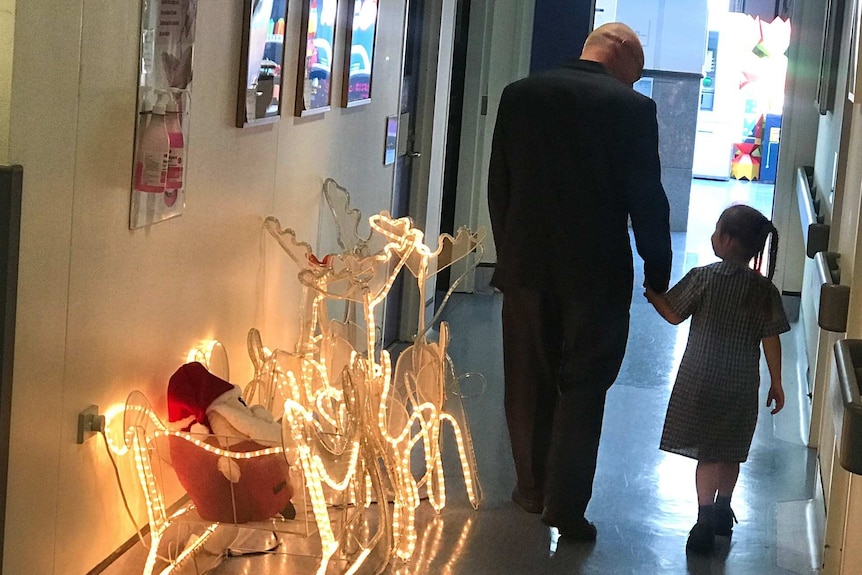 A man and a small girl walking down a corridor next to an illuminated reindeer.