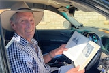 Farmer in driver's side of ute holding open book up, looking at the camera