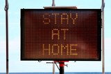 a sign saying stay at home on the beach where two people are hugging