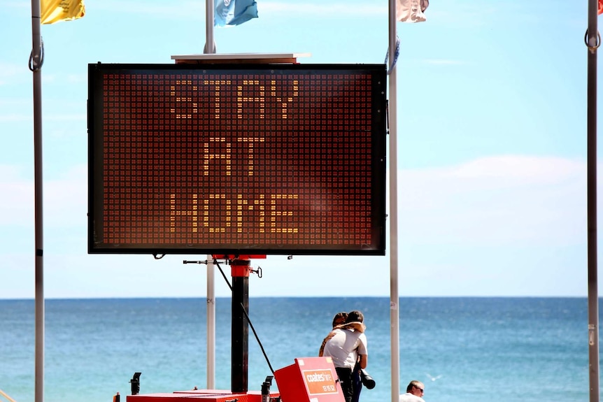 a sign saying stay at home on the beach where two people are hugging