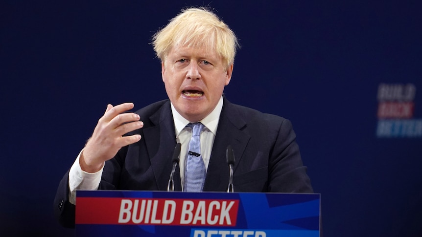 Boris Johnson stands at a podium, speaking while gesturing with his hand.