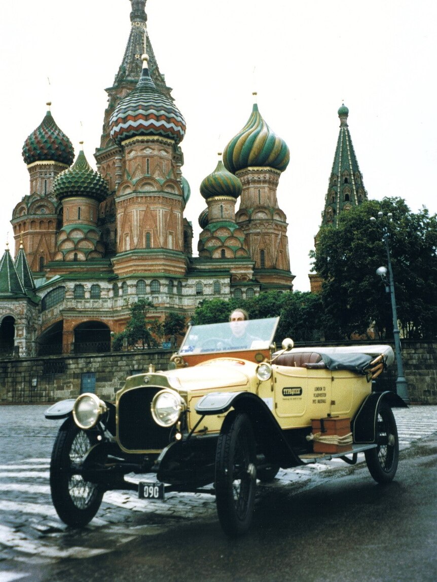 An old photo of Noel driving a vintage car in front of the colourful St Basil's cathedral in Moscow.