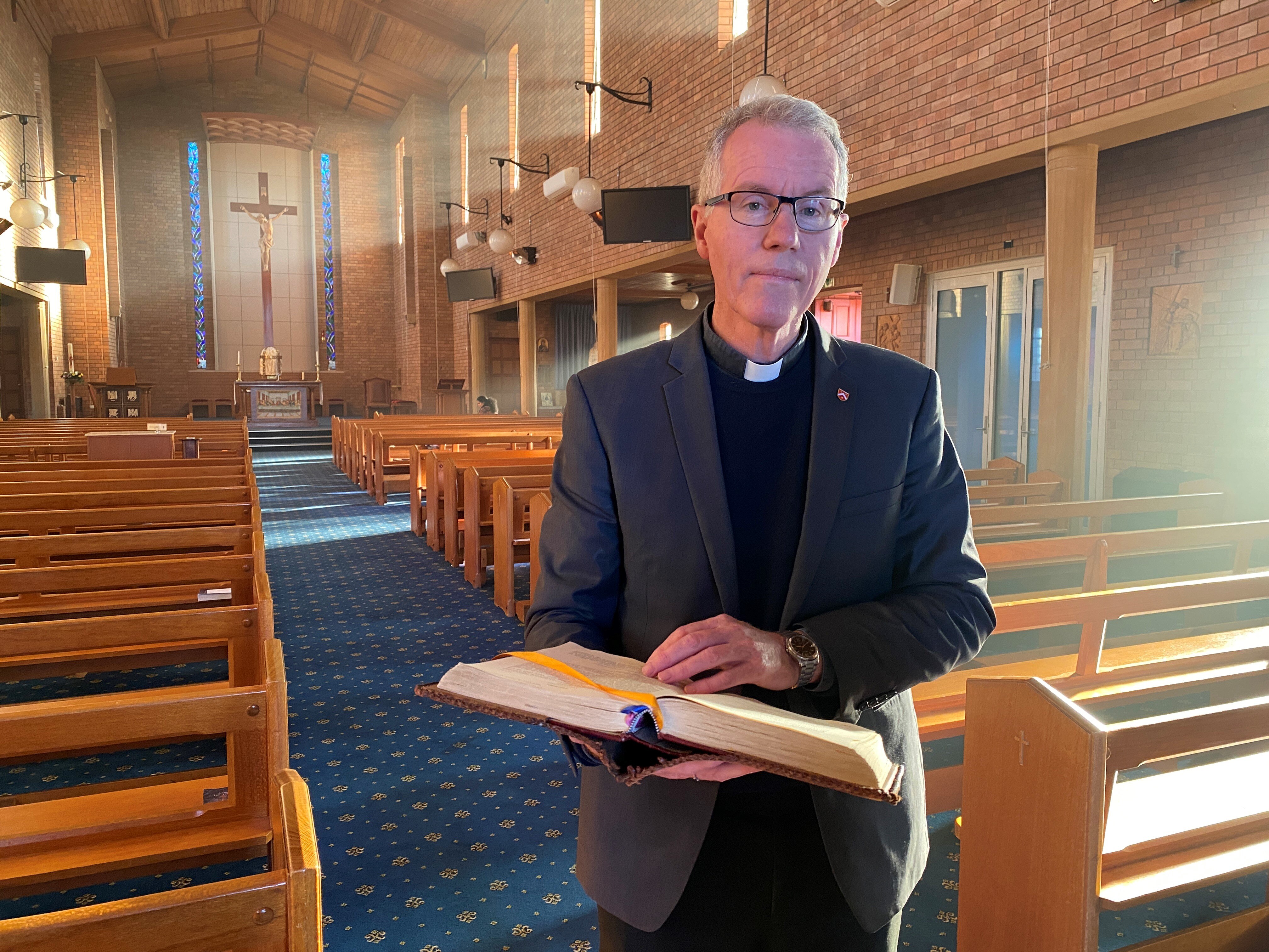 A Catholic priest holds an open bible in the middle of a church.