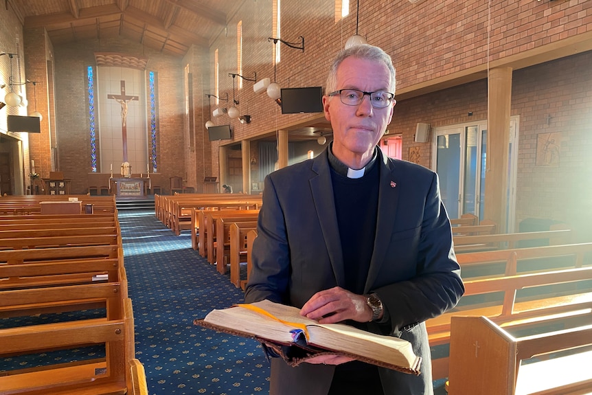 A Catholic priest holds an open bible in the middle of a church.