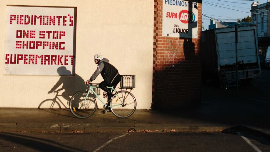 A woman rides by Piedimonte's Supermarket in Fiztroy North at sunrise.