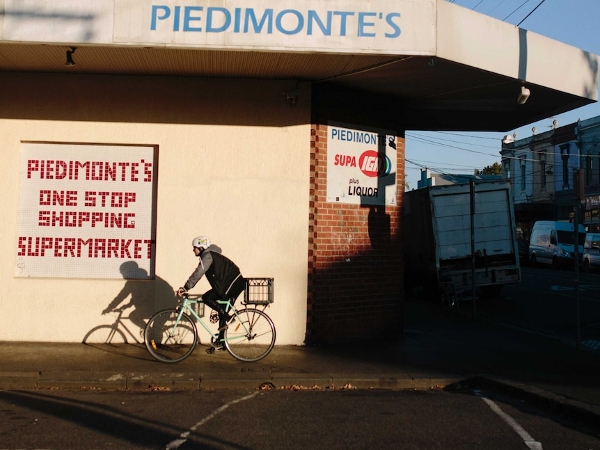 A woman rides by Piedimonte's Supermarket in Fiztroy North at sunrise.