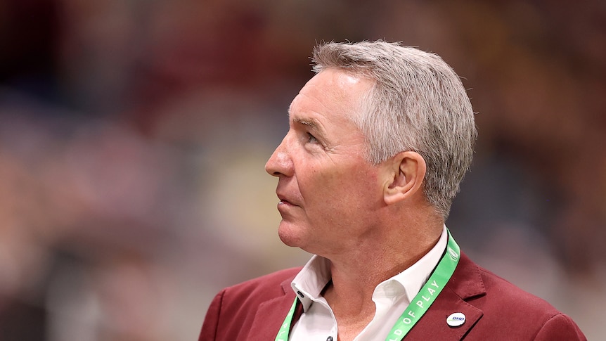 Paul Green looking up into the stands and smiling with a maroon jacket on. 