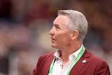 Paul Green looking up into the stands and smiling with a maroon jacket on. 
