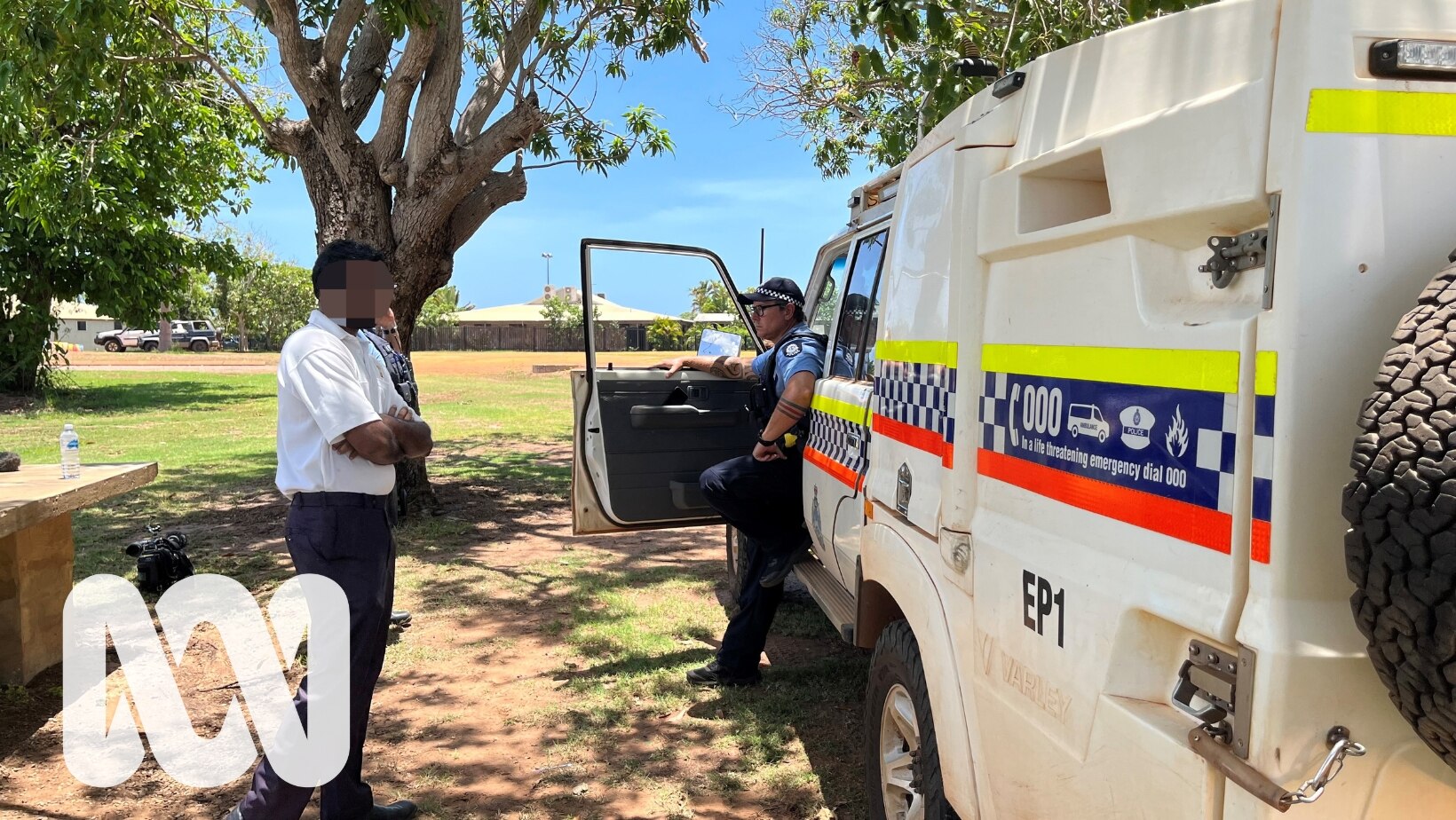 A man standing crossed arm next to a police officer and police car