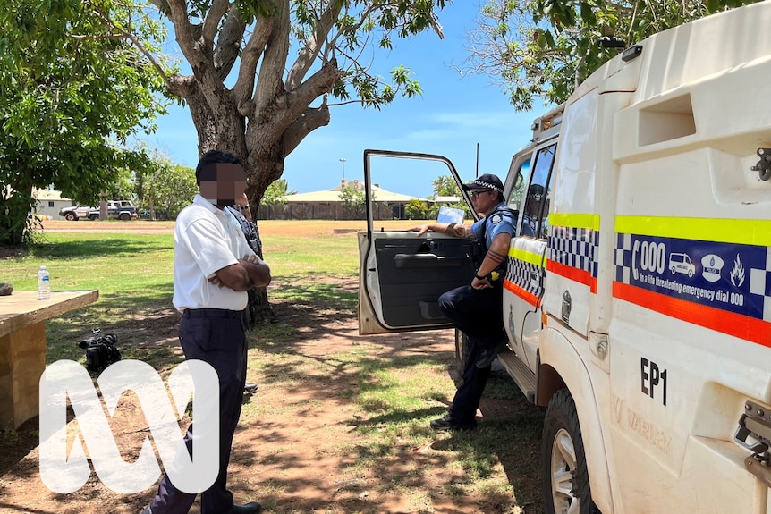 A man standing crossed arm next to a police officer and police car