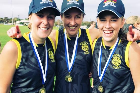 Three women in black and yellow football uniforms wearing medals