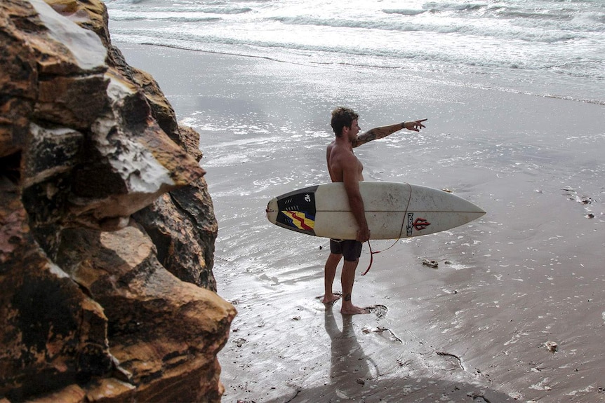 man pointing to the surf with his board