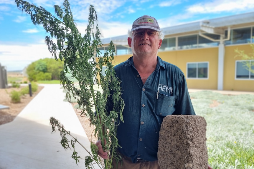 A man stands with a green plant in one hand, and a brick made from hemp in another.
