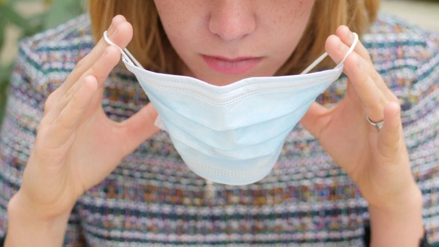 A woman raises a disposable mask towards her face.