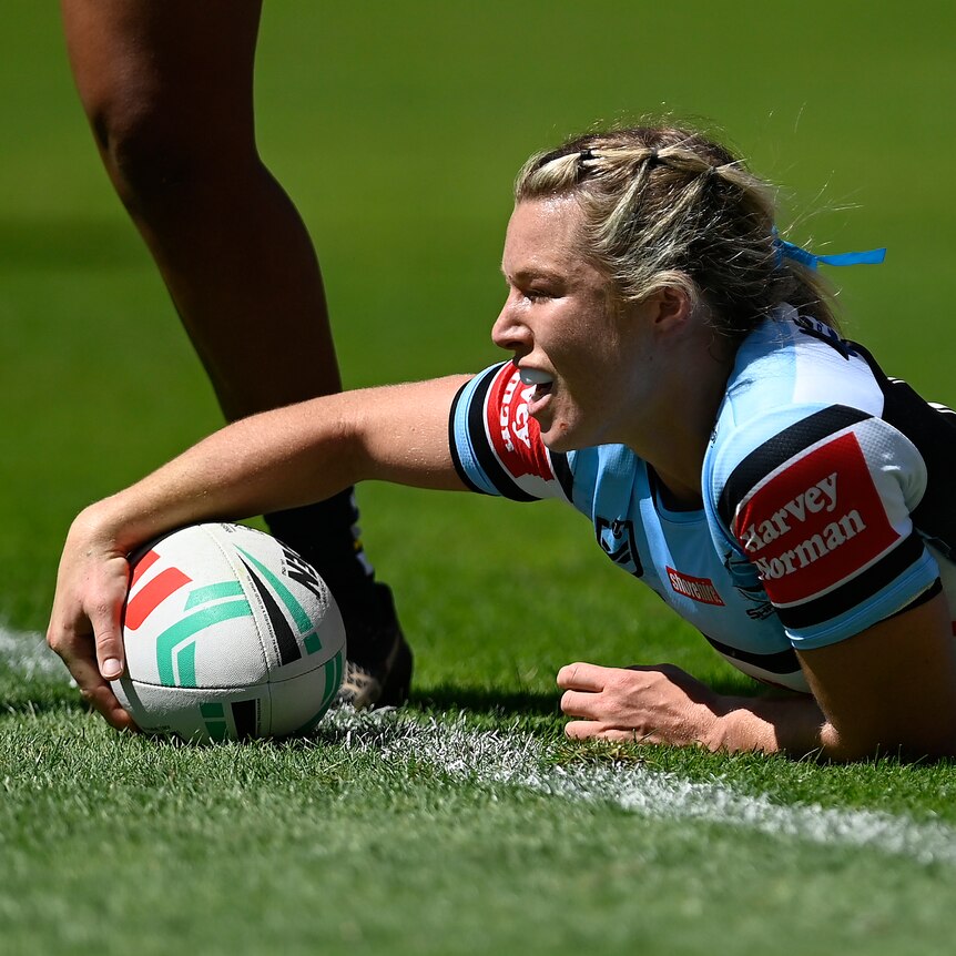 Emma Tonegato looks forward and places a rugby ball on the ground with one hand